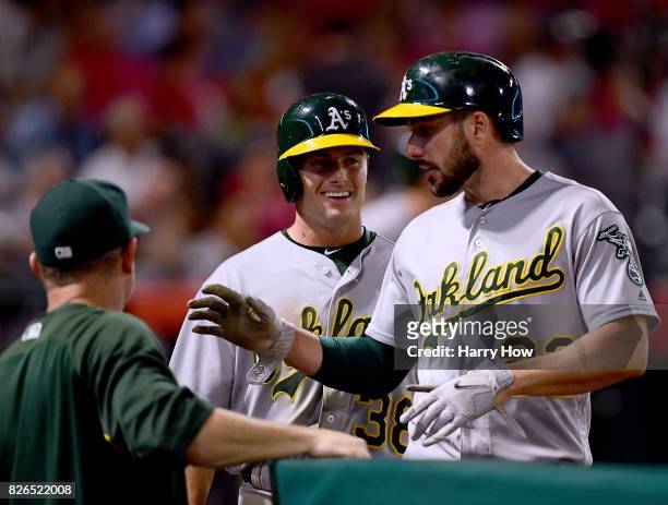 Jaycob Brugman and Matt Joyce of the Oakland Athletics smile as they come into the dugout, after scoring on a two run double from Khris Davis, to...