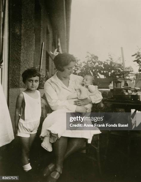 Baby Anne Frank in the arms of her mother Edith, with her older sister Margot standing nearby, June 1929.