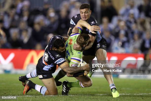 Clay Priest of the Raiders is tackled by Jayson Bukuya and Chris Heighington of the Sharks during the round 22 NRL match between the Cronulla Sharks...