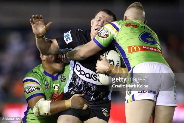 Paul Gallen of the Sharks is tackled by Josh Papalii and Blake Austin of the Raiders during the round 22 NRL match between the Cronulla Sharks and...