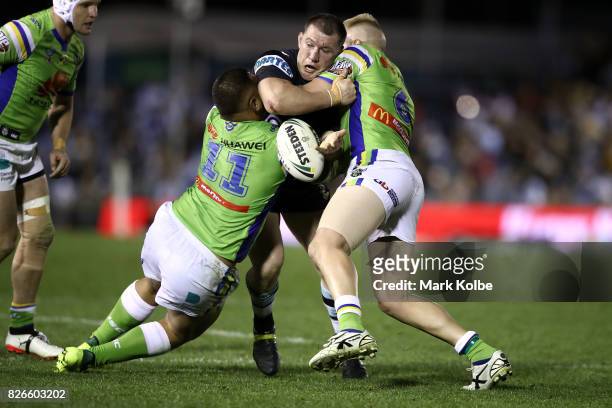 Paul Gallen of the Sharks tries to offlaod as he is tackled by Josh Papalii and Blake Austin of the Raiders during the round 22 NRL match between the...