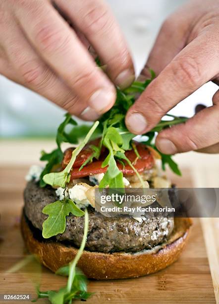 hands placing greens on burger - preparación de alimentos fotografías e imágenes de stock