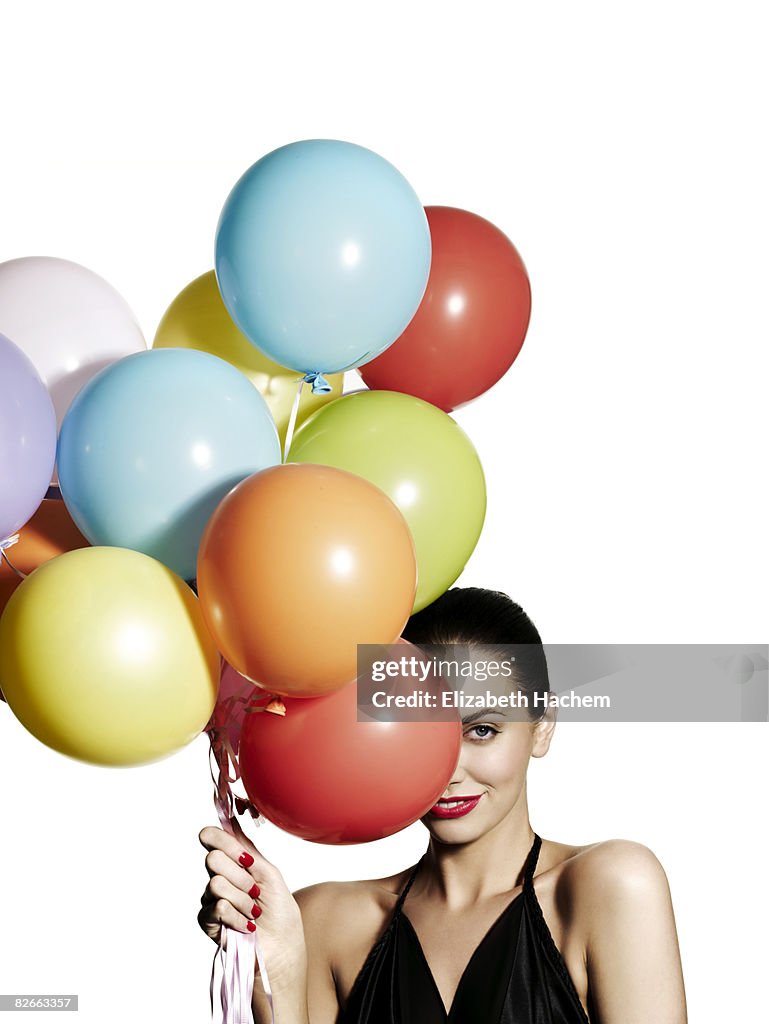 Girl hiding one eye behind a bunch of balloons