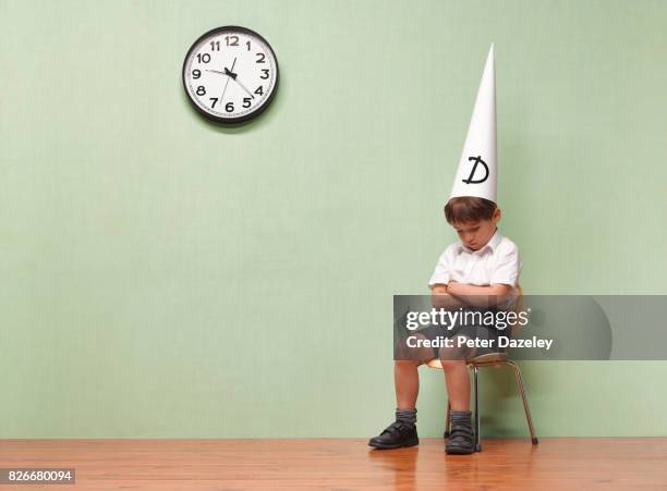 humiliated schoolboy with dunces hat in classroom - school punishment stockfoto's en -beelden