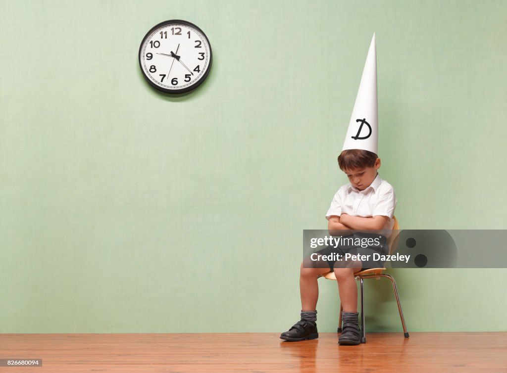 HUMILIATED SCHOOLBOY WITH DUNCES HAT IN CLASSROOM