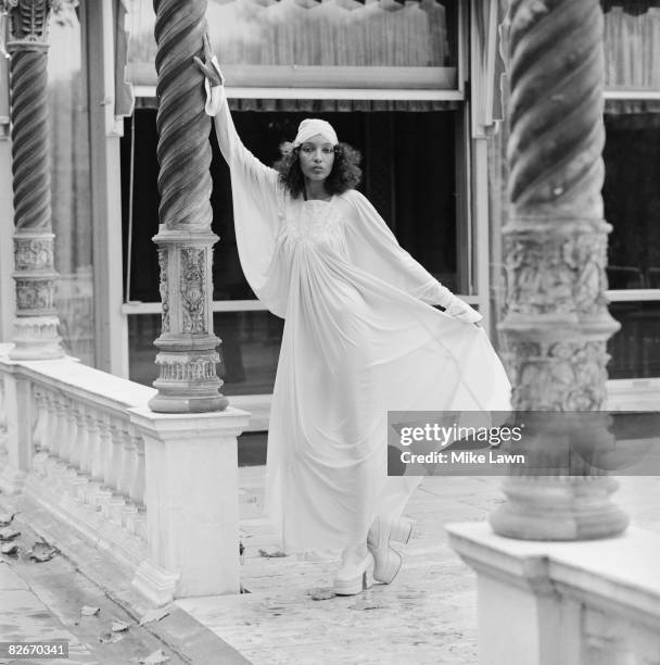 Model wearing a full-length white dress with matching hat, at a show by British designers Bill Gibb, John Bates, Jean Muir and Zandra Rhodes, at Les...