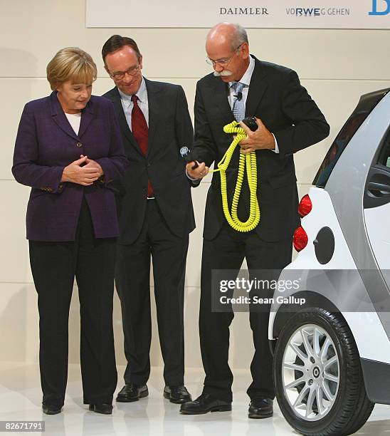 Daimler head Juergen Zetsche demonstrates how to plug in an electric-powered Smart car as German Chancellor Angela Merkel and Matthias Wissmann,...