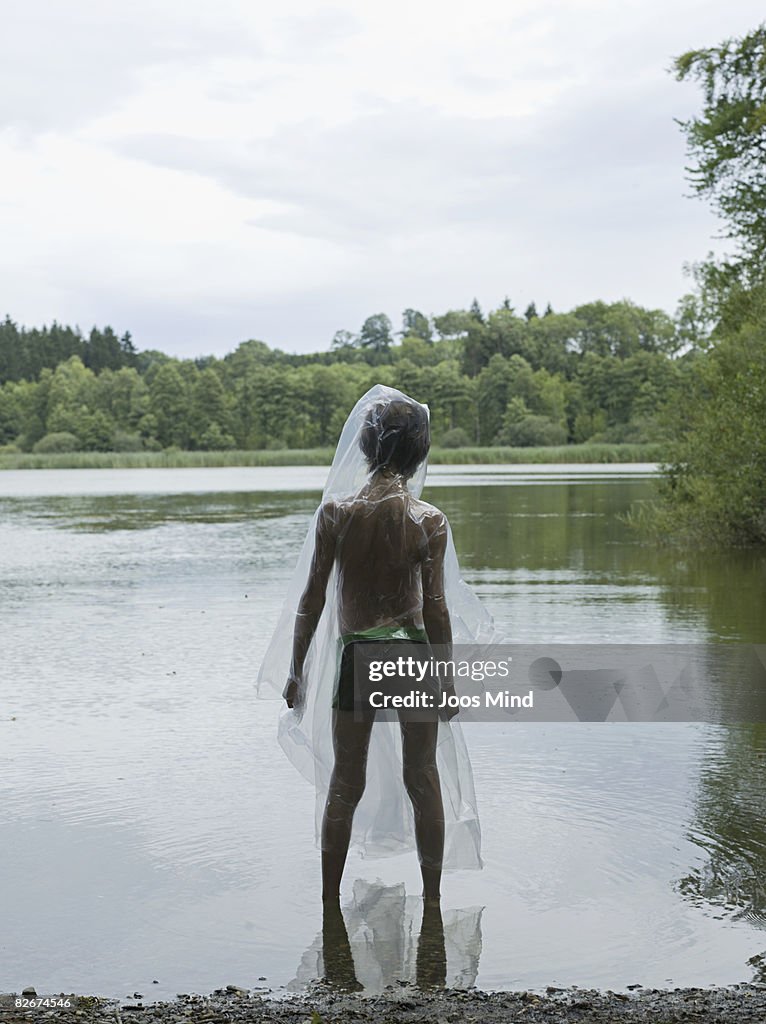 Boy wearing rain cape by lake, rear view