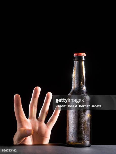 bottle of beer with the glass esmerilado with drops of water and the hand of a man with a hand gesture of four fingers on a black bottom - beer mat stockfoto's en -beelden