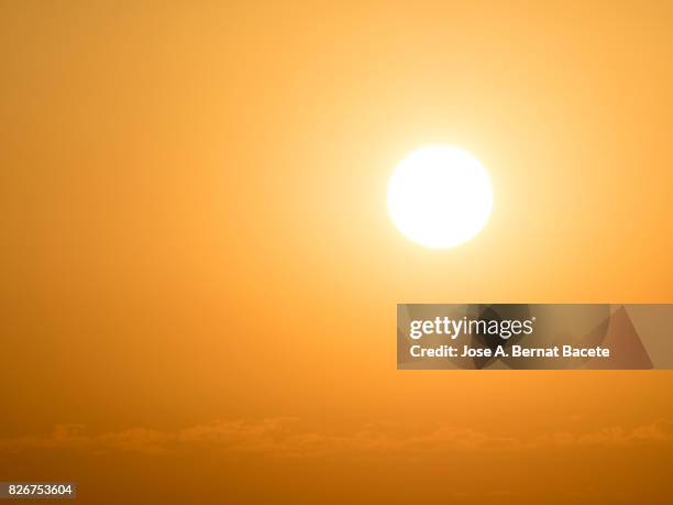 full frame glowing sun at sunset with an orange and yellow sky - orange couleur photos et images de collection