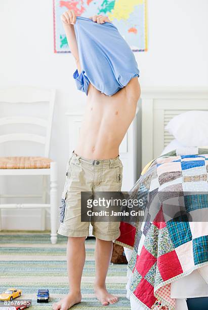 young boy taking off shirt in room - uitkleden stockfoto's en -beelden