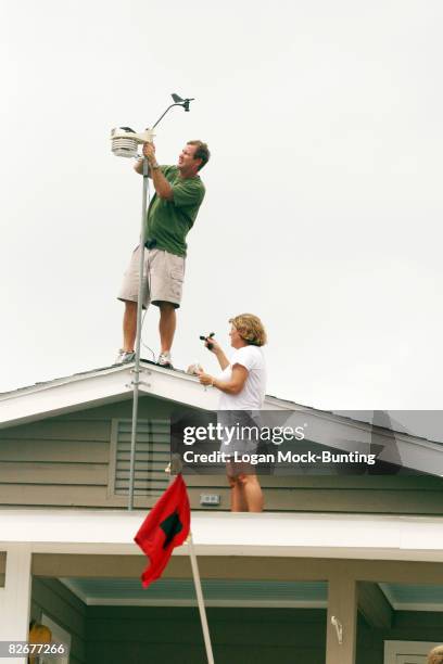 With a tropical Storm Warning flag flying in front of their house, Stanley and Boo Carraway prepare a weather station on their roof before the...