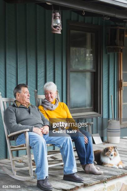 älteres paar sprechen auf veranda, lächelnd, mit hund - schaukelstuhl stock-fotos und bilder