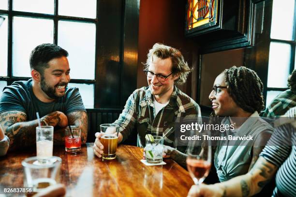 laughing friends in discussion while sharing drinks at table in bar - café bar 個照片及圖片檔