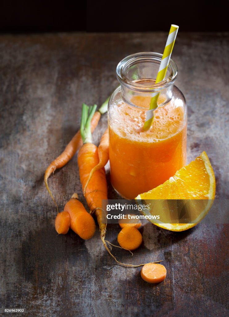 Carrot and orange juice on rustic wooden table top.