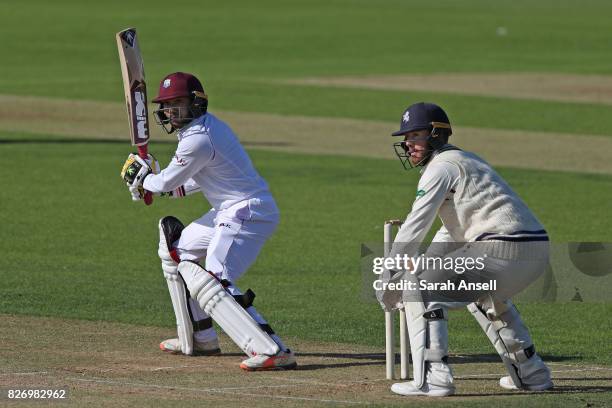 Devendra Bishoo of West Indies hits out as Kent wicket keeper Adam Rouse looks on during day one of the tour match between Kent and West Indies at...