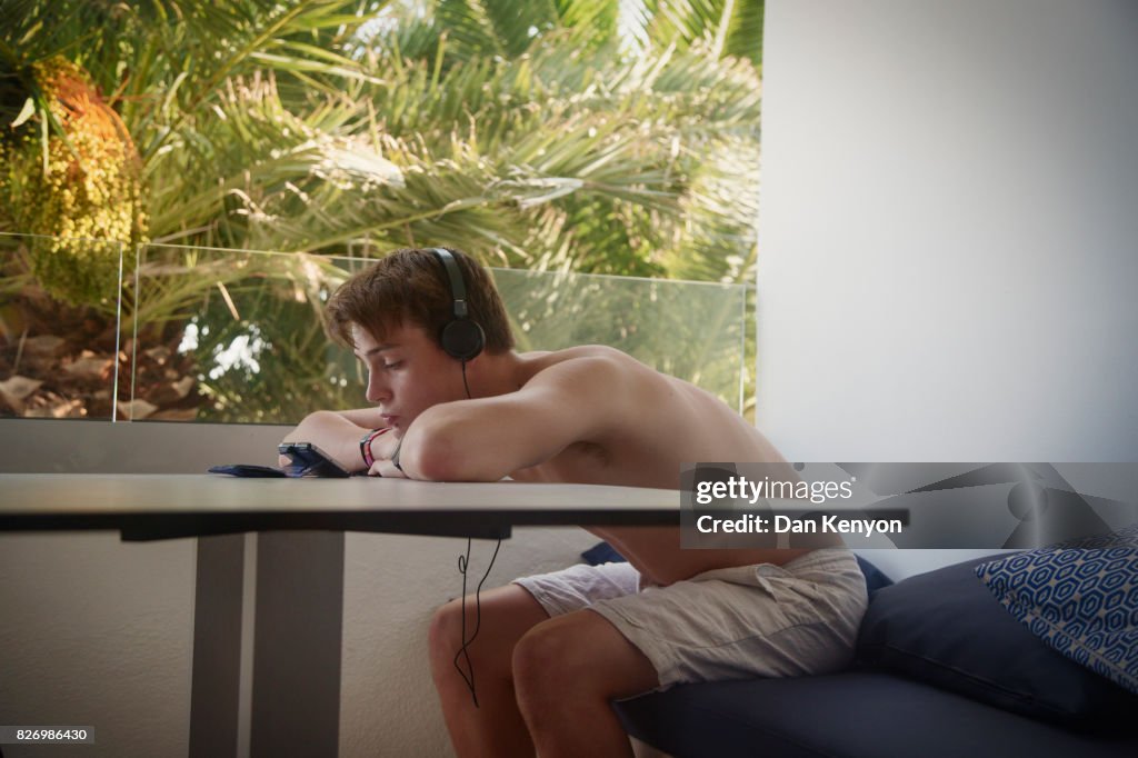 Teenage boy on hotel balcony watching film on phone.