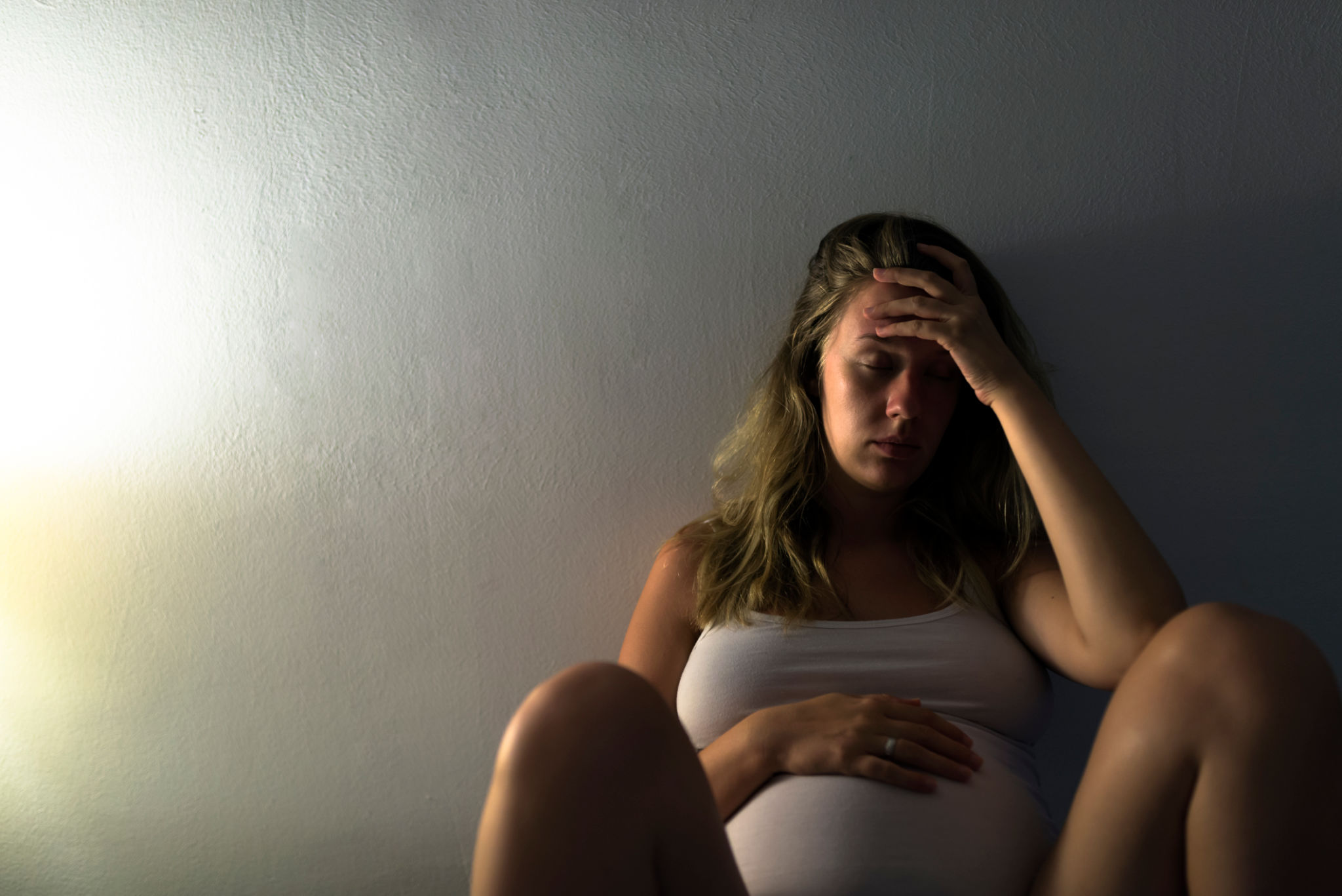 Sad Pregnant woman sitting on bed with her hand at belly Sad Pregnant woman sitting on bed with her hand at belly