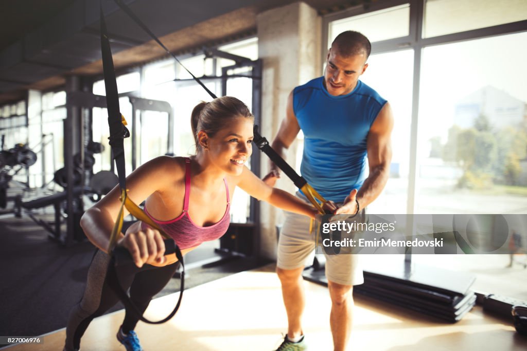 Woman doing arm exercises with suspension straps at gym.