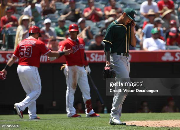 Pitcher Sean Manaea of the Oakland Athletics wipes his brow as Juan Graterol and Yunel Escobar of the Los Angeles Angels of Anaheim celebrate during...