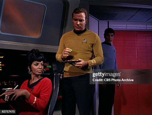 Watched by American actress Nichelle Nichols , Canadian actor William Shatner holds a plate on the bridge of the USS Enterprise in a scene from 'The...