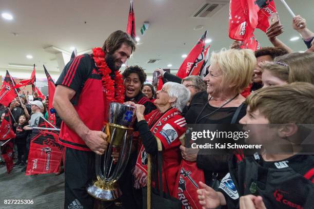 Captain Samuel Whitelock of the Crusaders presents the Super Rugby trophy to 95-year-old fan Doreen Searle during the Crusaders arrival at...