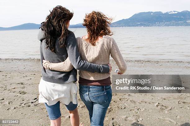 two girl walking towards water on beach - women side by side stock pictures, royalty-free photos & images