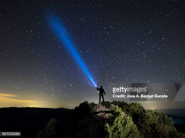silhouette of a man on the top of a mountain in the night, with a lantern in the hand doing a beam of light on a sky of stars - screaming man looking up stock-fotos und bilder