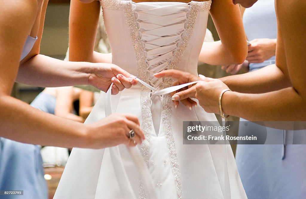 Bridesmaids help bride into her dress