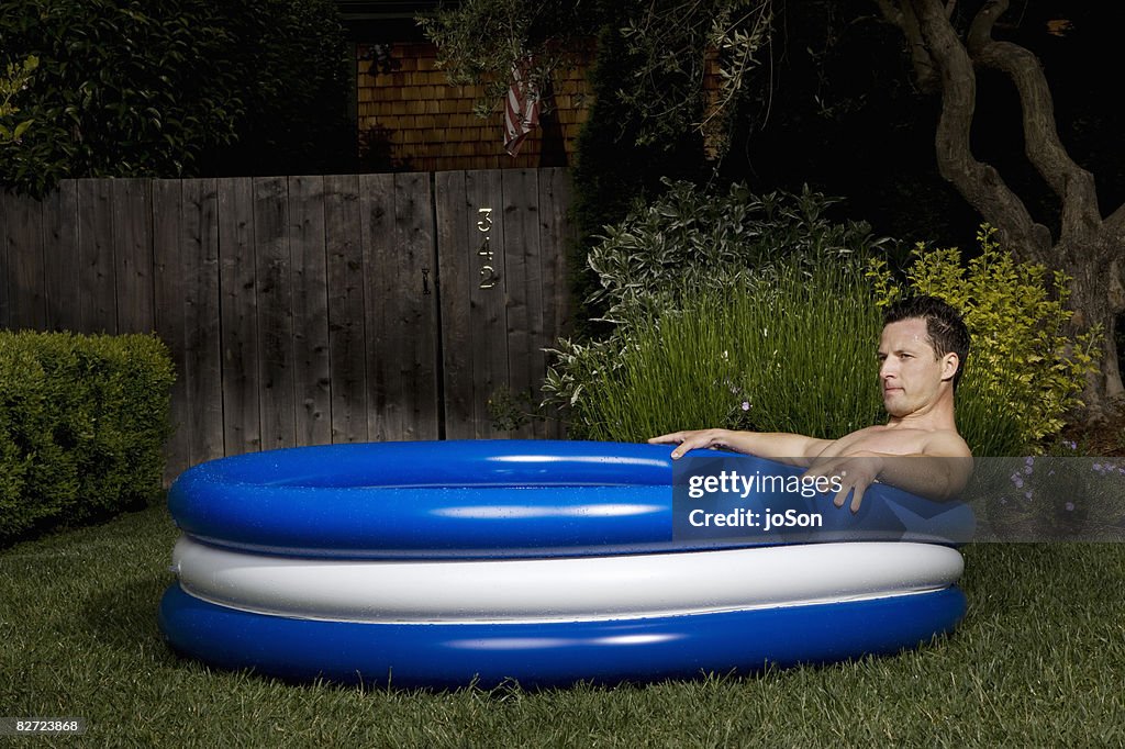 Man relaxing in vinyl kiddie paddling pool