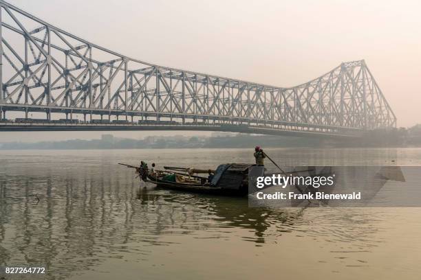 The steel construction of Howrah Bridge in Kolkata, a fishermans boat is crossing the Hoogli River.