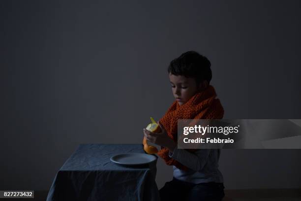 portrait of boy with orange scarf peeling an orange - chiaroscuro - fotografias e filmes do acervo