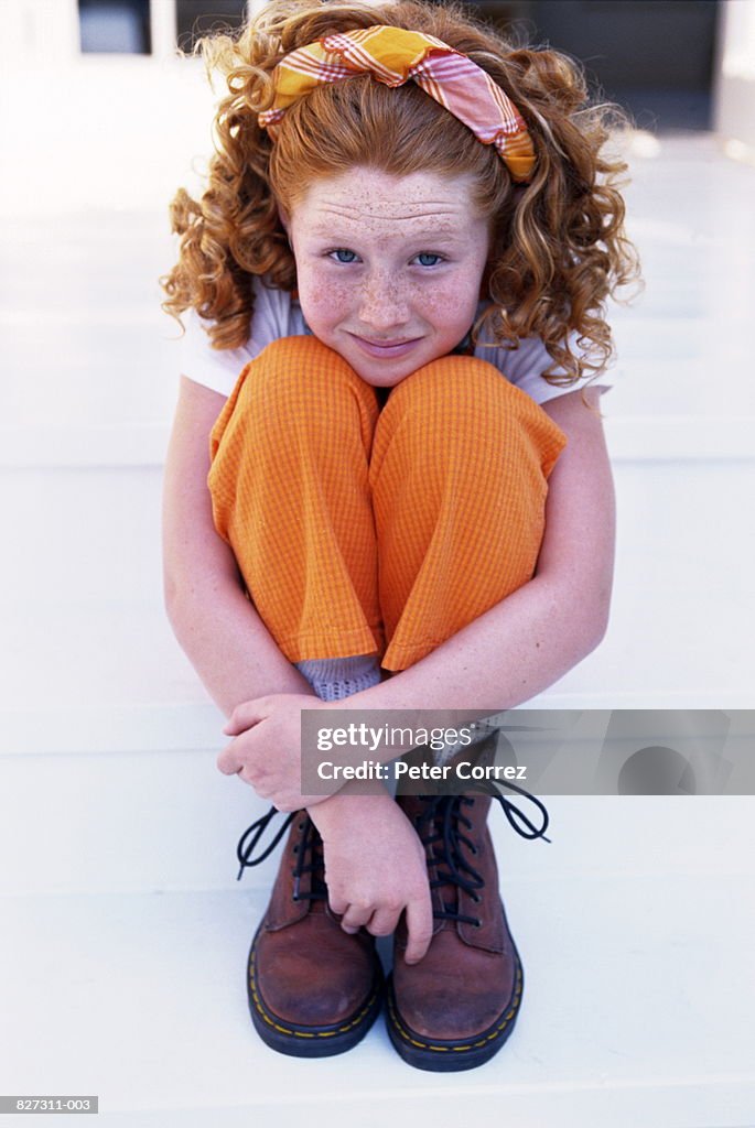 Young girl (6-8) sitting on steps, outdoors, portrait