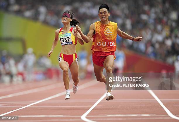 Partially sighted runner Wu Chunmiao of China runs to win gold with her guide in the final of the 100m T11 final A during the 2008 Beijing Paralympic...