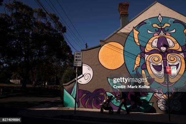 Pedestrain pushing a pram passes a large wall mural on the side of a house in Newtown on August 7, 2017 in Sydney, Australia. Perfect Match is an...