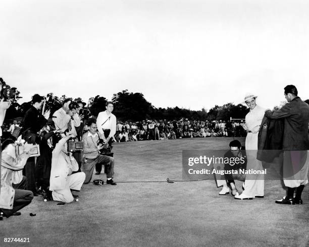 Sam Snead gets his first green jacket from Lloyd Mangrum as Johnny Bulla shines his shoes and a crowd of media photograph them during the...