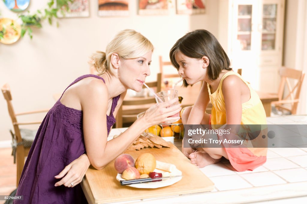 Mother and daughter drinking from same glass