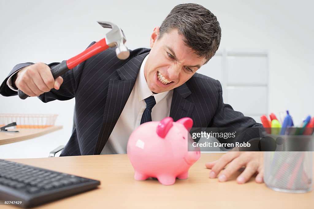 Businessman using hammer to smash open a piggybank