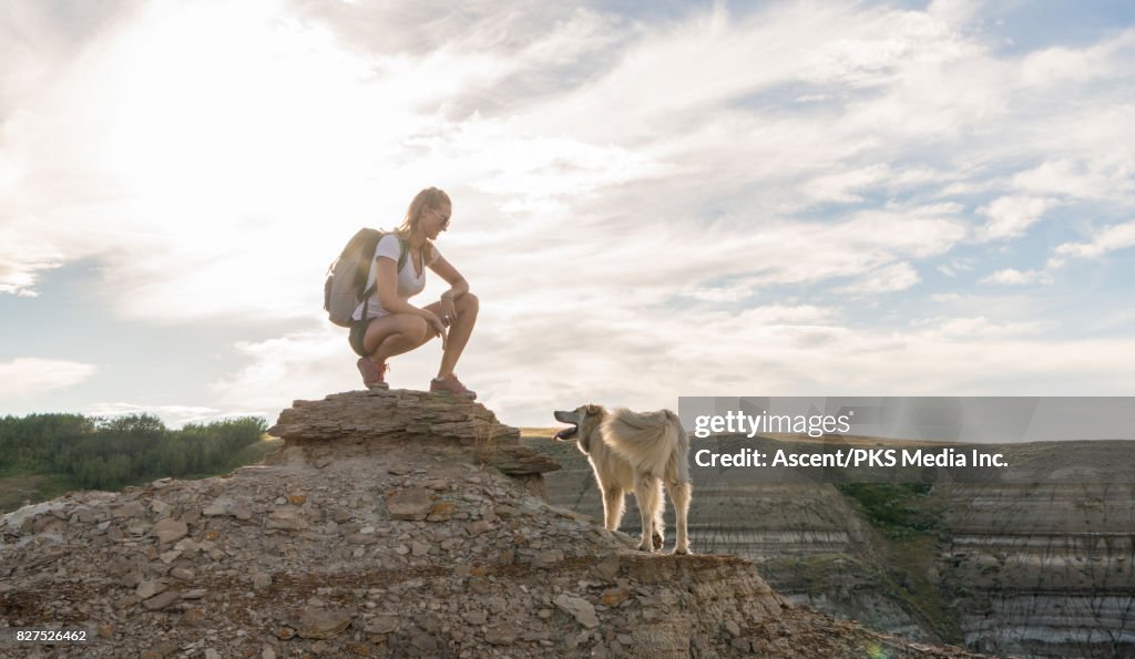 Woman pauses with dog on hillside above badlands