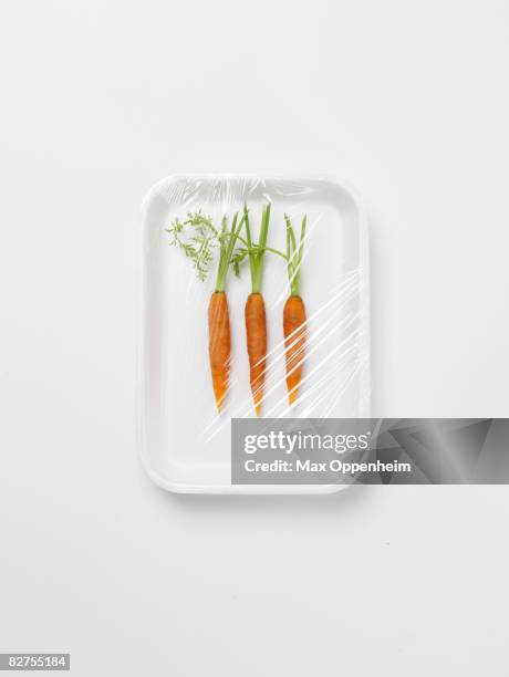 three baby carrots encased in plastic wrapping - plastic folie stockfoto's en -beelden
