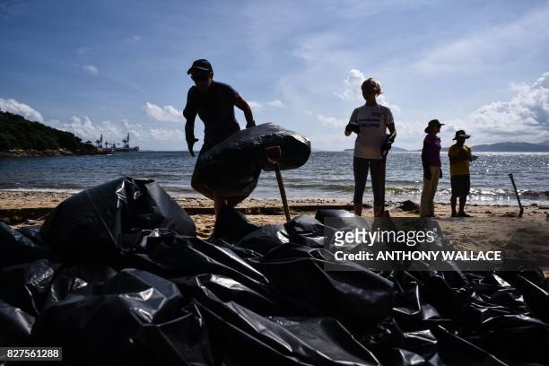 Volunteers help remove washed up palm oil from a beach in front of a pile of black bin bags on Hong Kong's outlying Lamma Island on August 8, 2017. -...