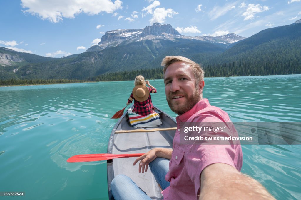 Young couple taking selfie on red canoe at lake