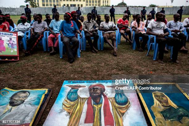 Alleged attackers sit behing paintings of Bundu Dia Mayala group leader Muanda Nsemiare on display at police headquarters in Kinshasa on August 8 a...