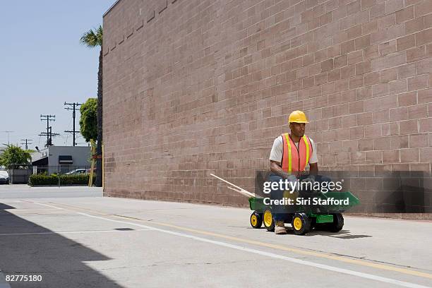 man in construction outfit on toy tractor - safety funny fotografías e imágenes de stock