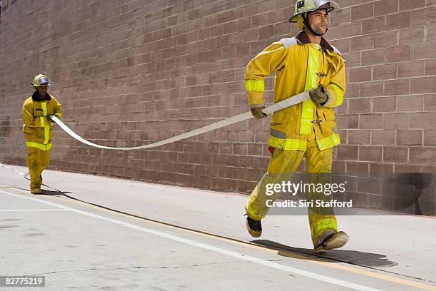 men in firefighter suits carrying hose - brandslang stockfoto's en -beelden