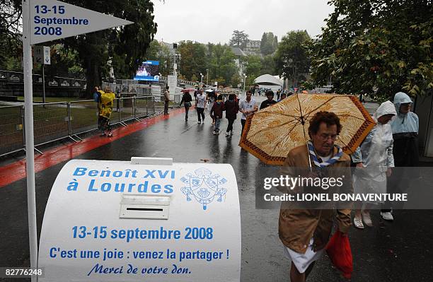 Pilgrims walk past a donation box in Lourdes on September 11, 2008 ahead of the visit of Pope Benedict XVI who will commemorate here the 150th...