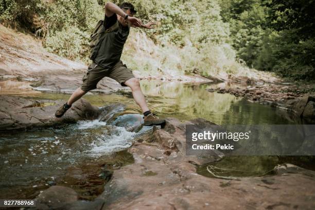 jonge man wandelen sprongen over de rivier van de berg - skip stockfoto's en -beelden
