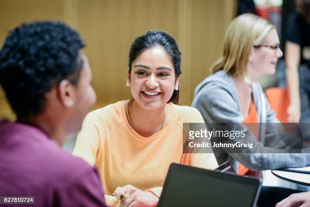 cheerful young woman listening to friend in college classroom, smiling - england stock pictures, royalty-free photos & images