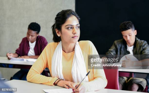 young woman in yellow sweater doing exam, looking away - indian college students imagens e fotografias de stock