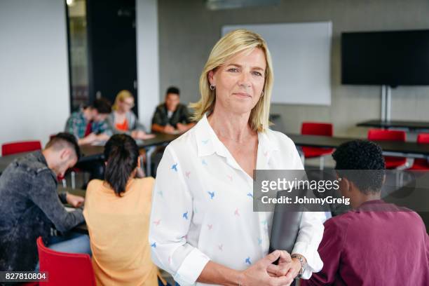 confident female lecturer in classroom holding folder, looking at camera - system demonstration stock pictures, royalty-free photos & images